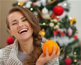 Portrait of smiling young woman with orange near Christmas tree