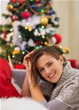 Smiling young woman sitting near Christmas tree