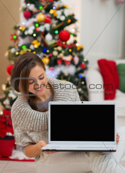 Happy woman looking laptop blank screen near Christmas tree