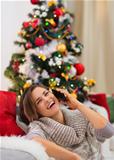 Smiling young woman speaking mobile near Christmas tree