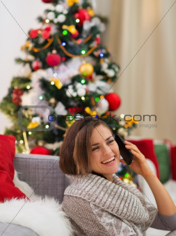 Happy young woman speaking mobile near Christmas tree