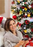 Happy young woman writing sms near Christmas tree