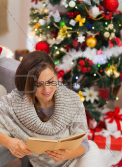 Happy young woman reading book near Christmas tree
