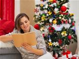 Young woman reading book near Christmas tree