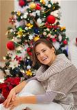 Portrait of happy young woman sitting near Christmas tree