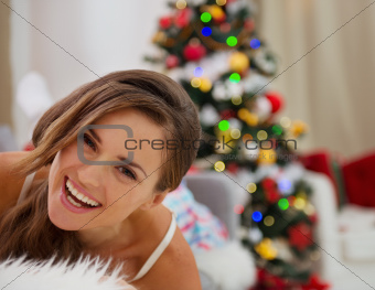 Smiling young woman in pajamas laying on couch near Christmas tree