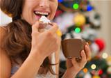 Closeup on young woman eating cookies with hot chocolate near Christmas tree