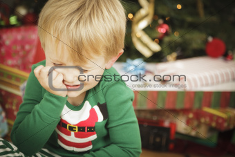 Grumpy Cute Young Boy on Christmas Morning Near The Tree.