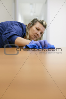 Professional female cleaner wiping table in office