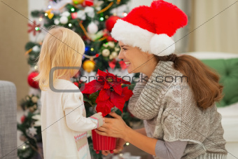 Mother and baby girl with Christmas rose near Christmas tree