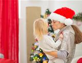Mother kissing baby in front of Christmas tree