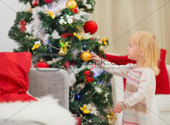 Baby touching Christmas ball on Christmas tree