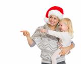 Happy mother in Christmas hat and baby girl pointing on copy space