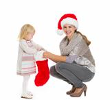 Happy mother holding Christmas sock while baby girl taking out present