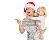 Smiling mother in Christmas hat and baby girl pointing on copy space