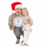 Happy mother in Christmas hat and baby girl holding clock
