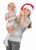 Smiling mother in Christmas hat and baby girl pointing up on copy space
