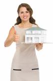Happy woman landlord with scale model of house showing thumbs up