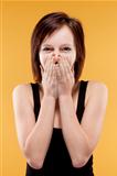 surprised teenage girl covering mouth with her hands looking, laughing - isolated on yellow