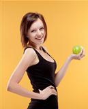 teenage girl holding a green apple smiling - isolated on yellow