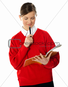 Cute school girl thinking and looking into notebook