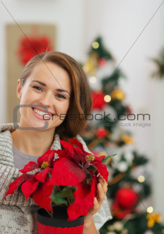 Happy woman holding Christmas rose in front of Christmas tree