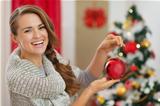 Smiling woman in front of Christmas tree holding Christmas ball