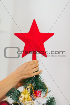 Closeup on woman hand decorating Christmas tree with topper