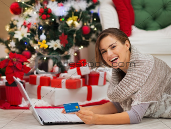 Happy woman with laptop near Christmas tree making online purchases