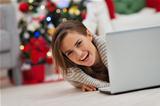 Smiling woman looking out from laptop in front of Christmas tree