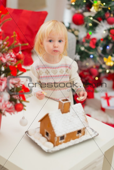 Portrait of baby eating cookies near Christmas Gingerbread house