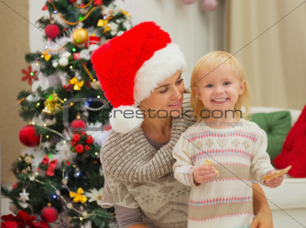 Portrait of mother and happy eat smeared baby near Christmas tree