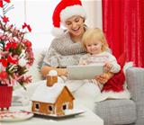 Mother showing baby something in tablet PC near Christmas tree