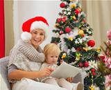 Happy mother and baby using tablet PC near Christmas tree