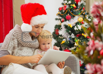 Mother and baby girl using tablet PC near Christmas tree