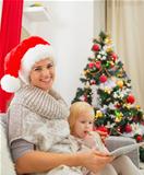 Smiling mother and baby girl using tablet PC near Christmas tree