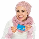 Smiling woman in knit scarf, hat and mittens holding credit card