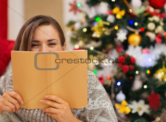 Woman hiding behind book in front of Christmas tree