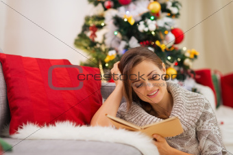 Woman reading book near Christmas tree