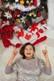 Happy woman laying near Christmas tree and pointing on copy space