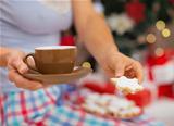 Closeup on woman in pajamas holding hot beverage and cookies in front of Christmas tree
