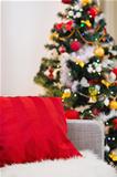 Closeup on sofa with red pillow in front of Christmas tree