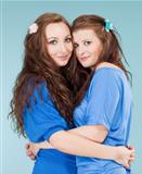 two young female friends hugging, looking - isolated on blue