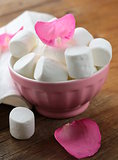 White  marshmallows  and pink rose petals on a wooden background