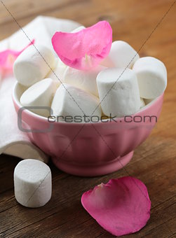 White  marshmallows  and pink rose petals on a wooden background