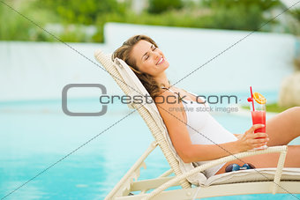 Young woman in swimsuit relaxing with cocktail on chaise-longue