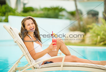 Smiling young woman in swimsuit relaxing with cocktail on chaise