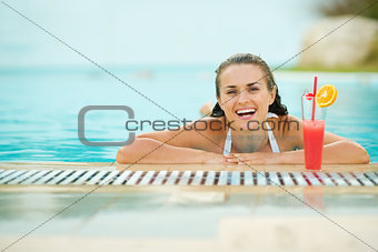 Smiling young woman relaxing in pool with cocktail
