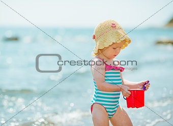 Baby playing with pail near sea