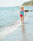 Happy baby with pail running along seashore